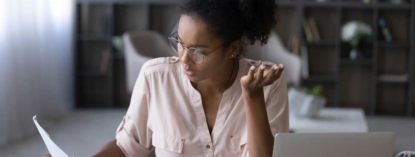 Stressed millennial generation african mixed race woman in eyewear looking at financial documents paper utility bills, feeling nervous about mistakes or bank loan rejection, bankruptcy concept.